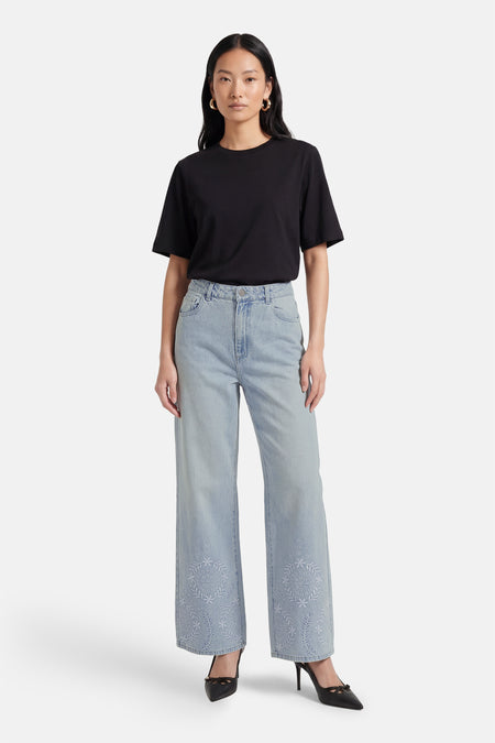 Lichtblauwe wijde jeans van Vero Moda, met geborduurde bloemen aan de onderkant, gecombineerd met een zwart T-shirt en zwarte pumps.
