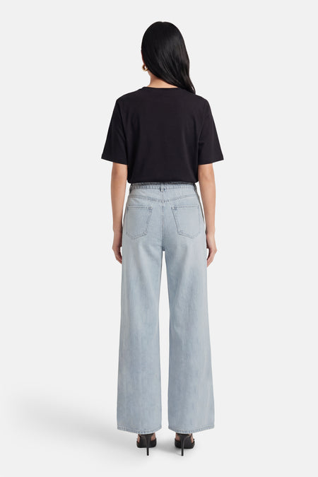 Lichtblauwe wijde jeans van VERO MODA®, gezien van achteren, gecombineerd met een zwart T-shirt en hakken.