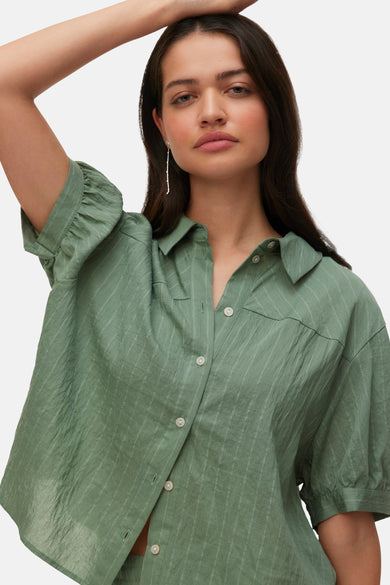 Chemisier vert à manches courtes de VERO MODA, avec fines rayures et texture froissée, porté par une femme dans le dos avec un pantalon et un bracelet assortis.