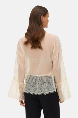 Blouse écru à longues manches de VERO MODA, avec des détails sur les bords et une jupe noire.