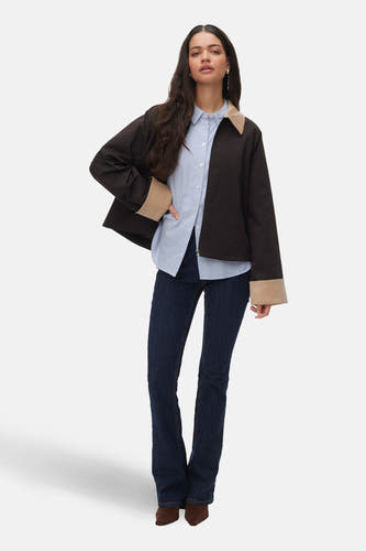 Bruine jas van VERO MODA, met beige kraag en manchetten, gedragen over een blauw gestreept overhemd en donkere jeans.
