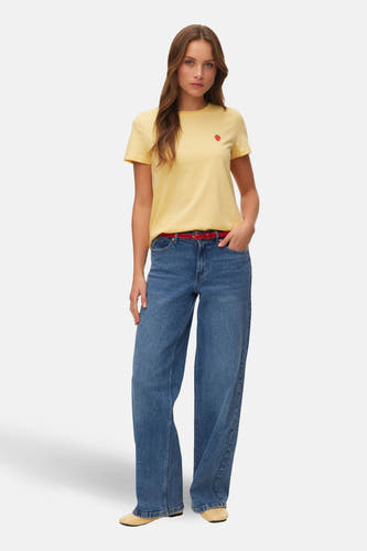 Geel T-shirt met korte mouwen van VERO MODA® met een kleine rode aardbei op de borst, gecombineerd met jeans en een rode riem.