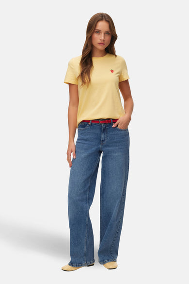 Geel T-shirt met korte mouwen van VERO MODA® met een kleine rode aardbei op de borst, gecombineerd met jeans en een rode riem.