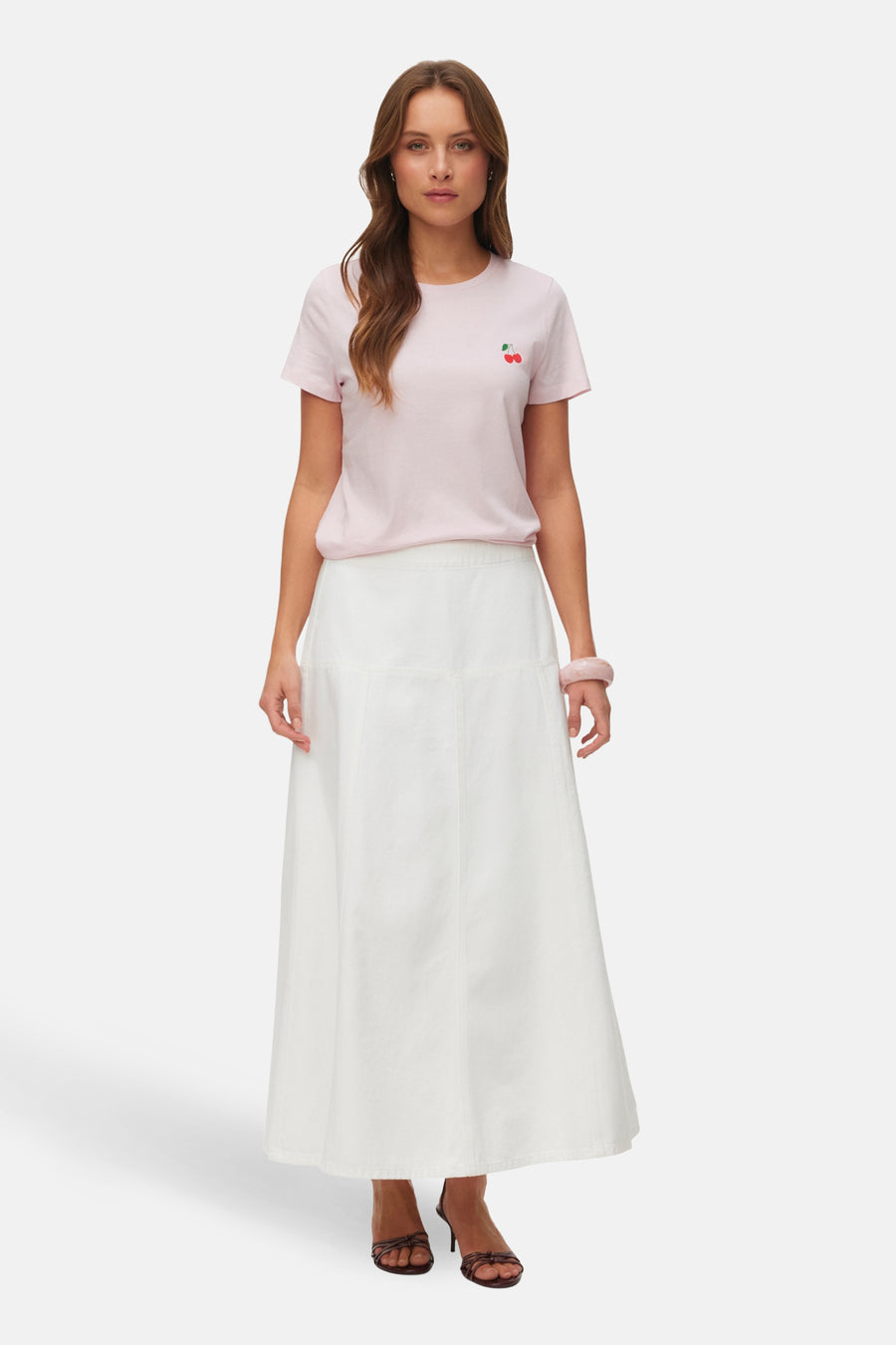 Roze T-shirt met korte mouwen van VERO MODA® met kersendetail, gecombineerd met een witte lange rok en bruine hakken.
