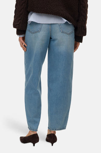 Lichte blauwe spijkerbroek van VERO MODA met wijde pijpen, grote achterzakken en opgerolde zomen, gedragen met een bruine trui en suède hakken, achterkant.