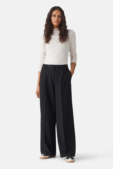 Zwarte broek van OPUS met wijde pijpen en plooien, gedragen door een model met een lichtgekleurde top en sneakers.