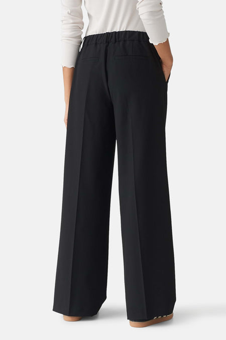 Zwarte broek van OPUS met elastische tailleband, zijzakken en wijde pijpen, achterkant, gedragen met witte top en bruine schoenen.