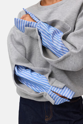 Grijze ronde hals sweater met multicolor gestreepte binnenkant van VERO MODA®, gedragen over een blauw-wit gestreept shirt, close-up op de zakken.