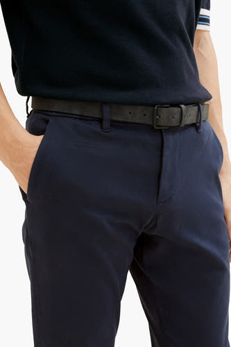Jean chino bleu de TOM TAILOR, avec une ceinture noire et une main dans la poche.