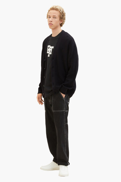 Zwarte gilet van TOM TAILOR, gedragen over een zwart T-shirt met print en donkere jeans, met witte sneakers.
