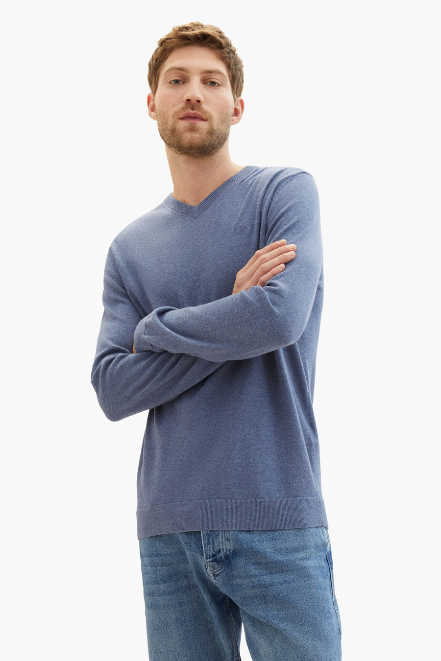 Man met gekruiste armen in blauwe trui en spijkerbroek, productfoto.