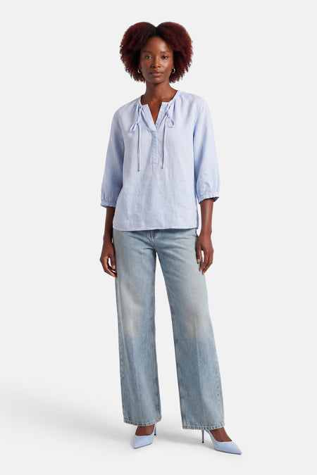 Chemisier bleu à manches longues OPUS, avec des nœuds au col et associé à un jean et des escarpins bleus.