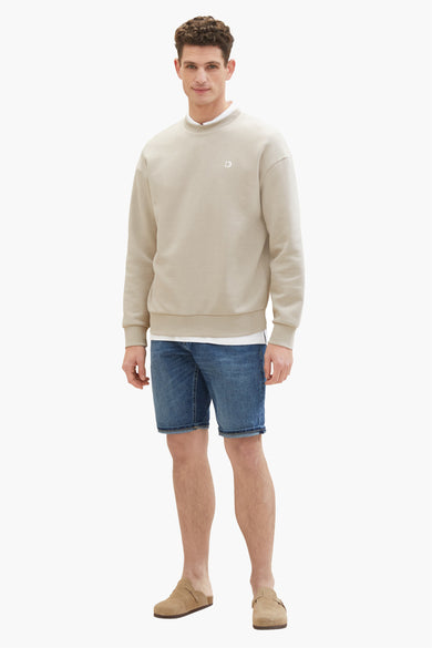 Jean en denim court dans le bleu marine, de TOM TAILOR, associé à un sweat-shirt beige et des mocassins en cuir.
