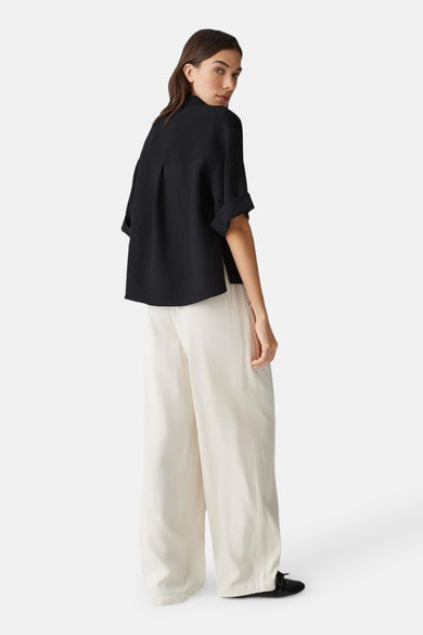 Chemise noire à manches courtes d'OPUS, portée avec un pantalon beige large.