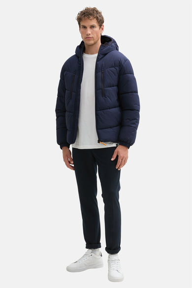 Manteau bleu court de TOM TAILOR, avec capuche et fermeture éclair noire, porté avec un pantalon foncé.