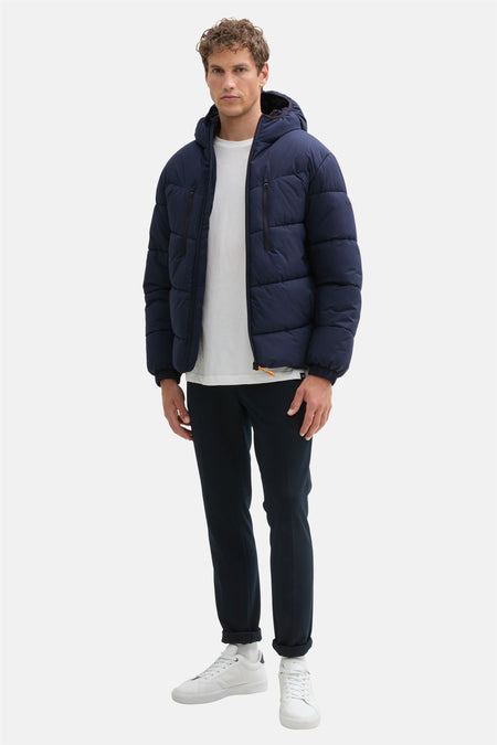 Manteau bleu court de TOM TAILOR, avec capuche et fermeture éclair noire, porté avec un pantalon foncé.
