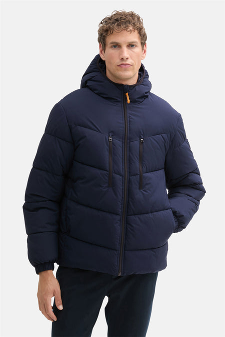 Korte blauwe jas van TOM TAILOR, met capuchon en zwarte ritssluiting, gedragen met donkere broek.