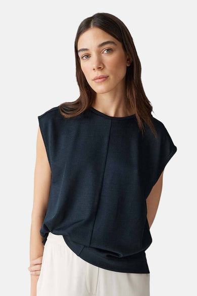 Blouse sans manches noire d'OPUS, avec une couture verticale et associée à un pantalon blanc.