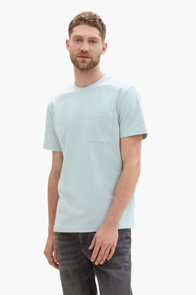 T-shirt vert de mantes courtes cour TOM TOMOROR, avec une poche poitrine port porté un pantalon de jeans gris.
