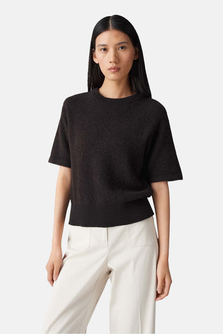 Pull marron OPUS, avec des manches courtes et une fine structure côtelée en bas, porté avec un pantalon blanc.