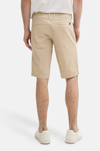 Een man van achteren gezien, gekleed in beige shorts en witte schoenen.