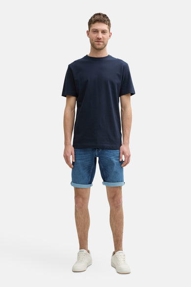 Jeansshort van midblauw denim van TOM TAILOR, met opgerolde zoom, gecombineerd met een donkerblauw T-shirt en witte sneakers.