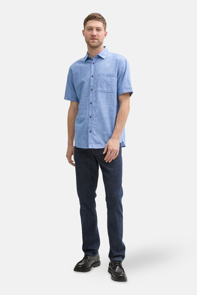Chemise bleue à manches courtes de TOM TAILOR, avec col boutonné et poche poitrine, associée à des jeans foncés et des chaussures noires.