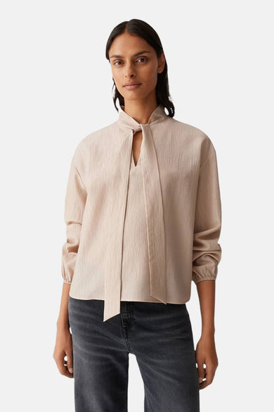 Blouse beige à longues manches d'OPUS, avec détail rayé et texture subtile, associée à un jean gris.