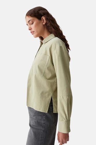 Blouse verte avec des manches longues d'OPUS, avec une poche poitrine et et poche latérale, portée avec un pantalon gris.