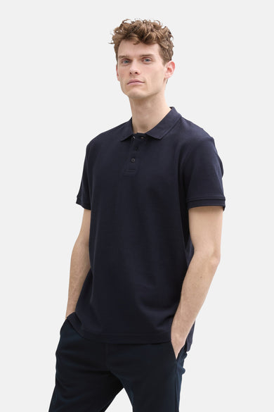 Polo bleu marine à manches courtes de TOM TAILOR, associé à un pantalon foncé et des baskets blanches.