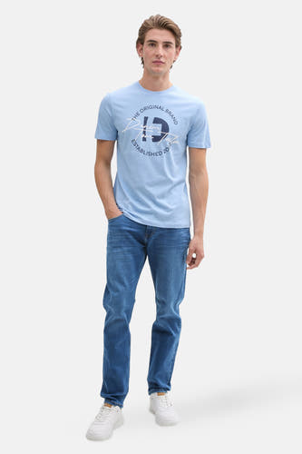 Slim fit jeans mid blue denim van TOM TAILOR, gecombineerd met een lichtblauw T-shirt en witte sneakers.