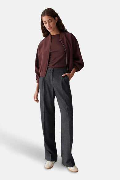 Pantalon noir d'OPUS, avec une subtile texture et une forme classique, droite, porté avec un gilet brun.