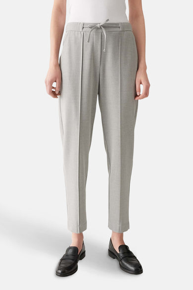 Pantalon gris OPUS, avec une fermeture éclair et porté avec des loafers noirs.