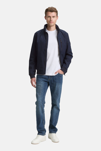 Manteau bleu court de TOM TAILOR, porté avec un t-shirt blanc et des jeans, le main dans la poche.