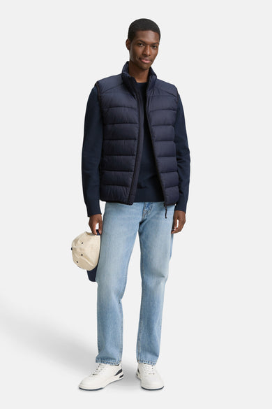 Gilet bleu de TOM TAILOR, porté sur une chemise bleue marine, associé à des jeans légers et des baskets blanches.