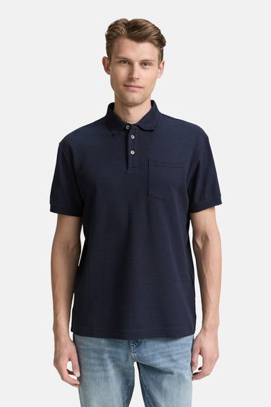 Polo bleu à manches courtes de TOM TAILOR, avec une poche po poitrine et porté avec un jeans bleu.