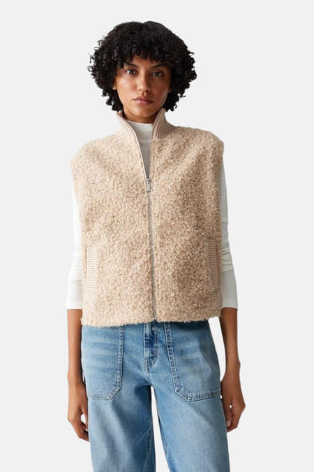 Couleur écru tricotée ronde avec OPUS, hals rond, portée sous un pull en fleece sans manches Teddy avec fermeture et jeans bleus.