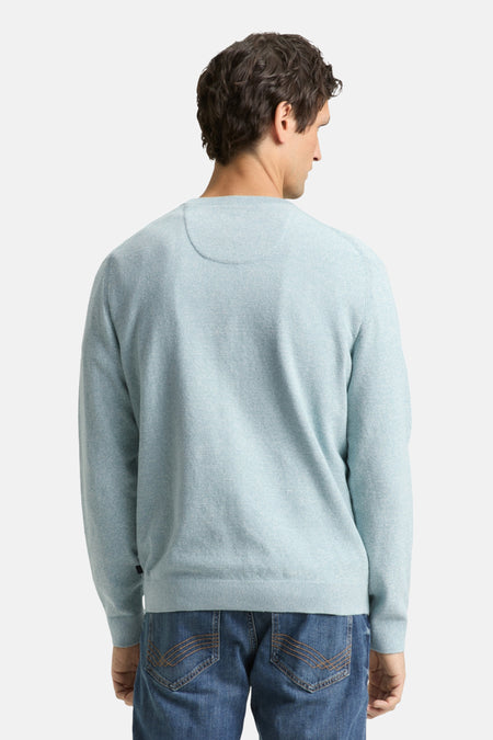 Achterkant van een man in een lichtblauwe trui en blauwe jeans.