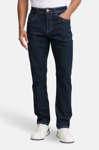 Jean slim fit en denim bleu marine de TOM TAILOR, avec une main dans la poche et des baskets blanches.