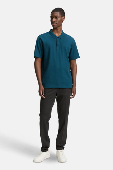 Een man in een blauw poloshirt, donkere broek en witte sneakers.