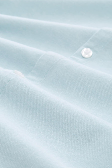 Close-up van een lichtblauw overhemd met knopen en plooien.
