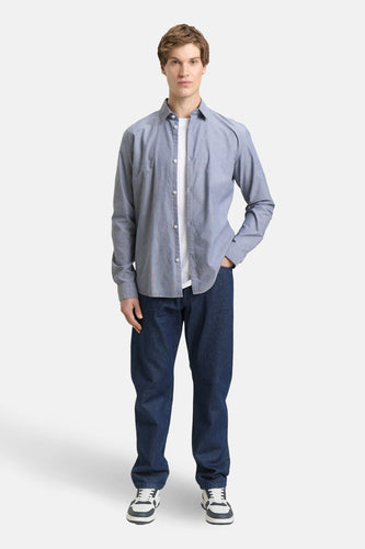 Man met open overhemd, jeans en sneakers, staand.
