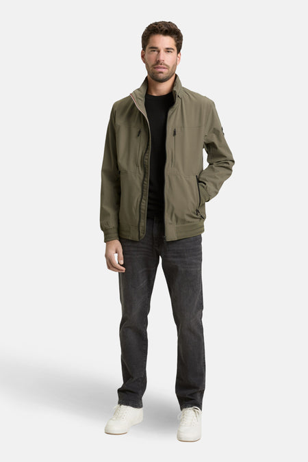 Man in olijfgroene jas, zwarte jeans en witte sneakers.
