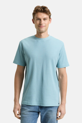 Man in lichtblauw geribbeld T-shirt en jeans op witte achtergrond.