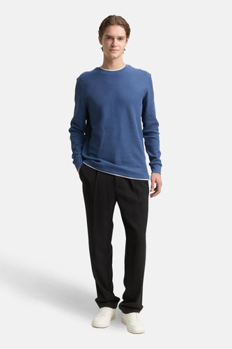 Man in blauwe trui en zwarte broek.