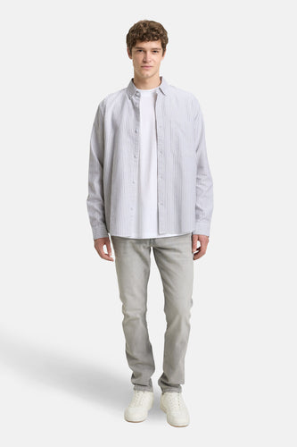 Staande man in wit t-shirt, gestreept overhemd, grijze jeans en witte sneakers.