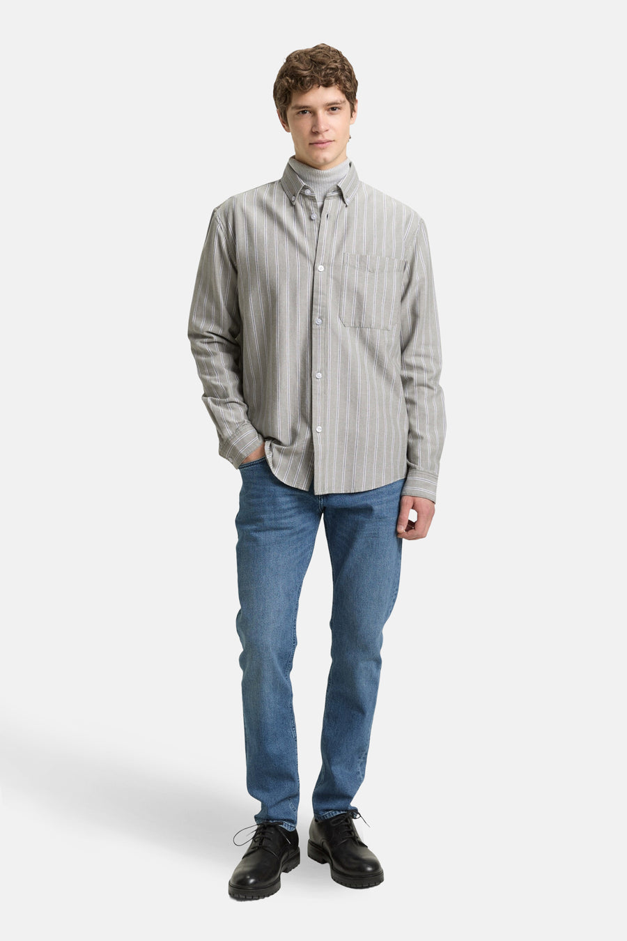 Een man in jeans en een gestreept overhemd.