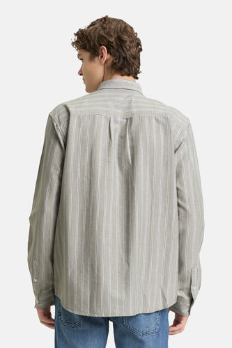 Man met krullend haar van achteren gezien in gestreept overhemd en blauwe jeans.