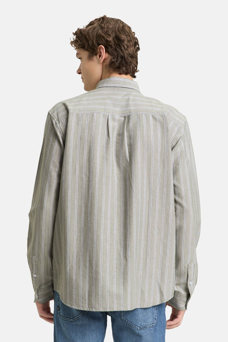 Man met krullend haar van achteren gezien in gestreept overhemd en blauwe jeans.