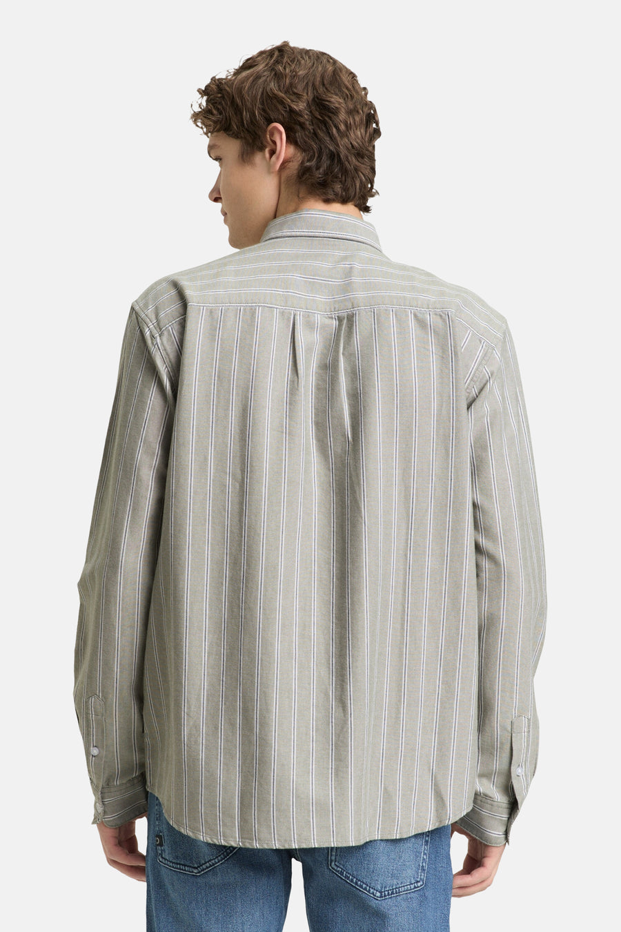 Man met krullend haar van achteren gezien in gestreept overhemd en blauwe jeans.